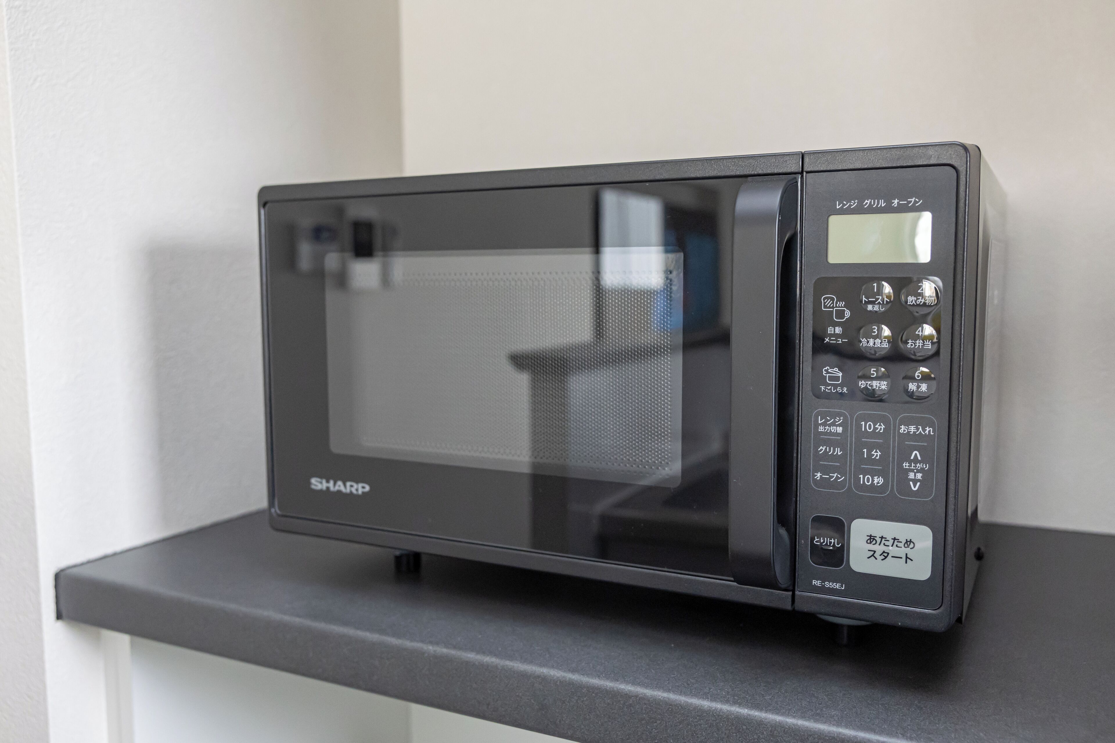 Un four à micro-ondes noir de la marque Sharp, posé sur un plan de travail.