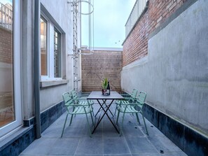 A small outdoor patio with a table and chairs, a potted plant, and a window.