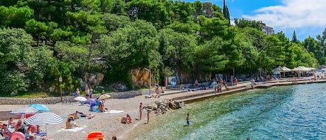 A beach with clear water, people sunbathing, and umbrellas.