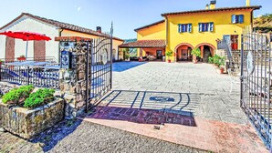Ein Innenhof mit befestigtem Bereich, einem Tor und einem Gebäude mit gelbem Putz und blauen Fensterläden.