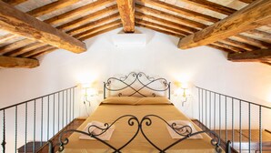 Ein Schlafzimmer mit Holzboden, einem Bett mit Metallgestell, zwei Wandleuchten und einer Treppe mit Geländer.