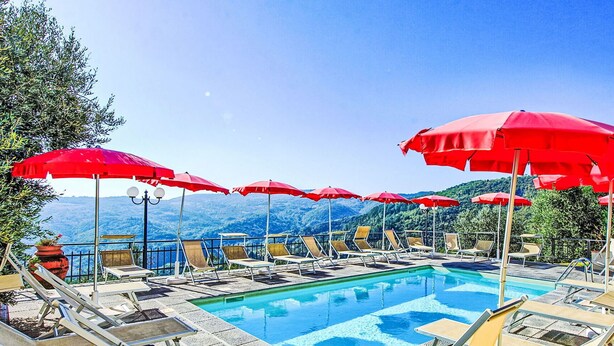 Ein Poolbereich mit roten Sonnenschirmen, Liegestühlen und Blick auf die Berge.
