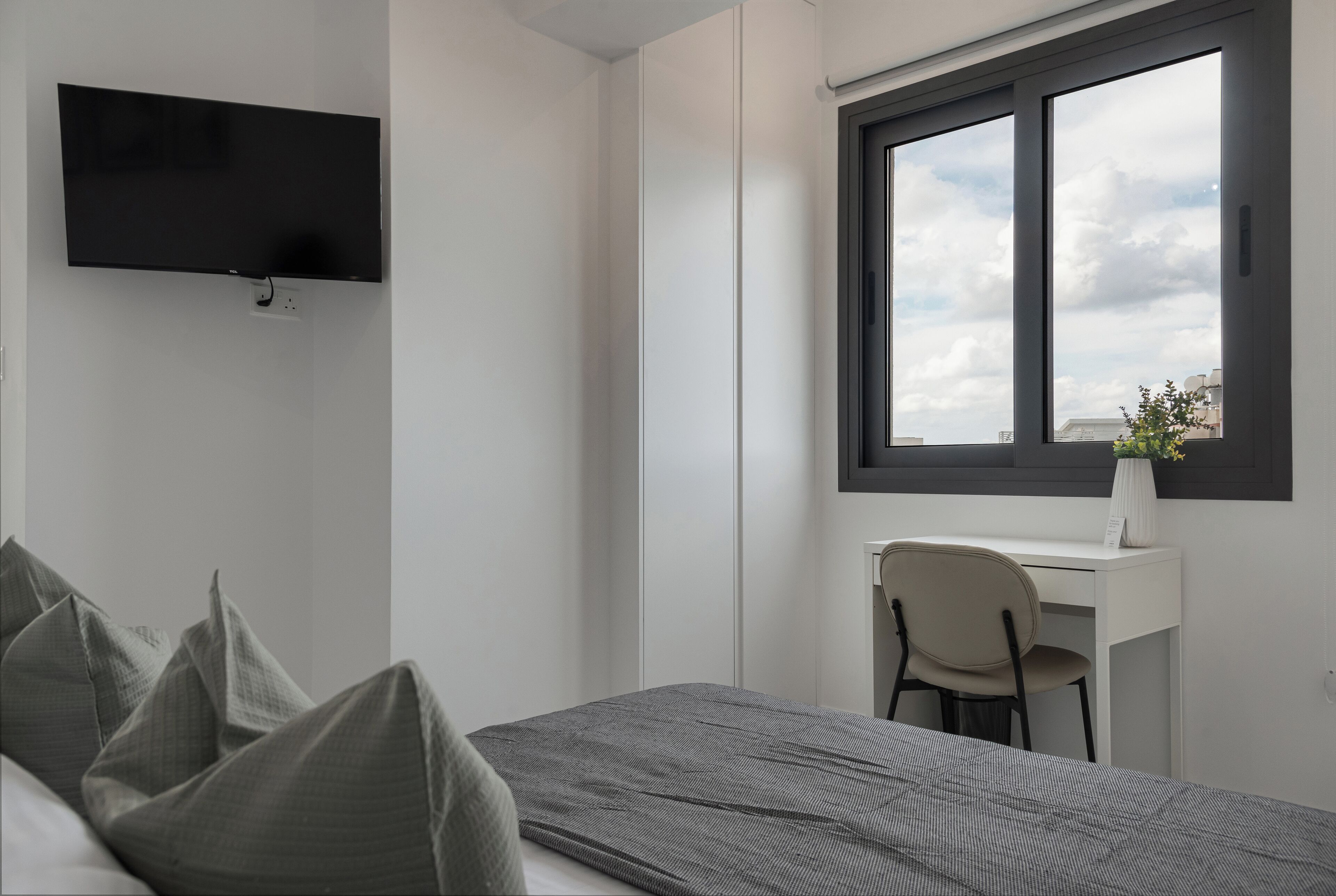 A modern bedroom with a bed, a desk, and a TV.