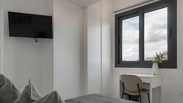 A modern bedroom with a bed, a desk, and a TV.