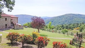 A stone building with a red roof, surrounded by a well-maintained lawn and colorful flowering shrubs. - Stunning private villa for 8 people with WIFI, private pool, patio and pets allowed (Cortona)