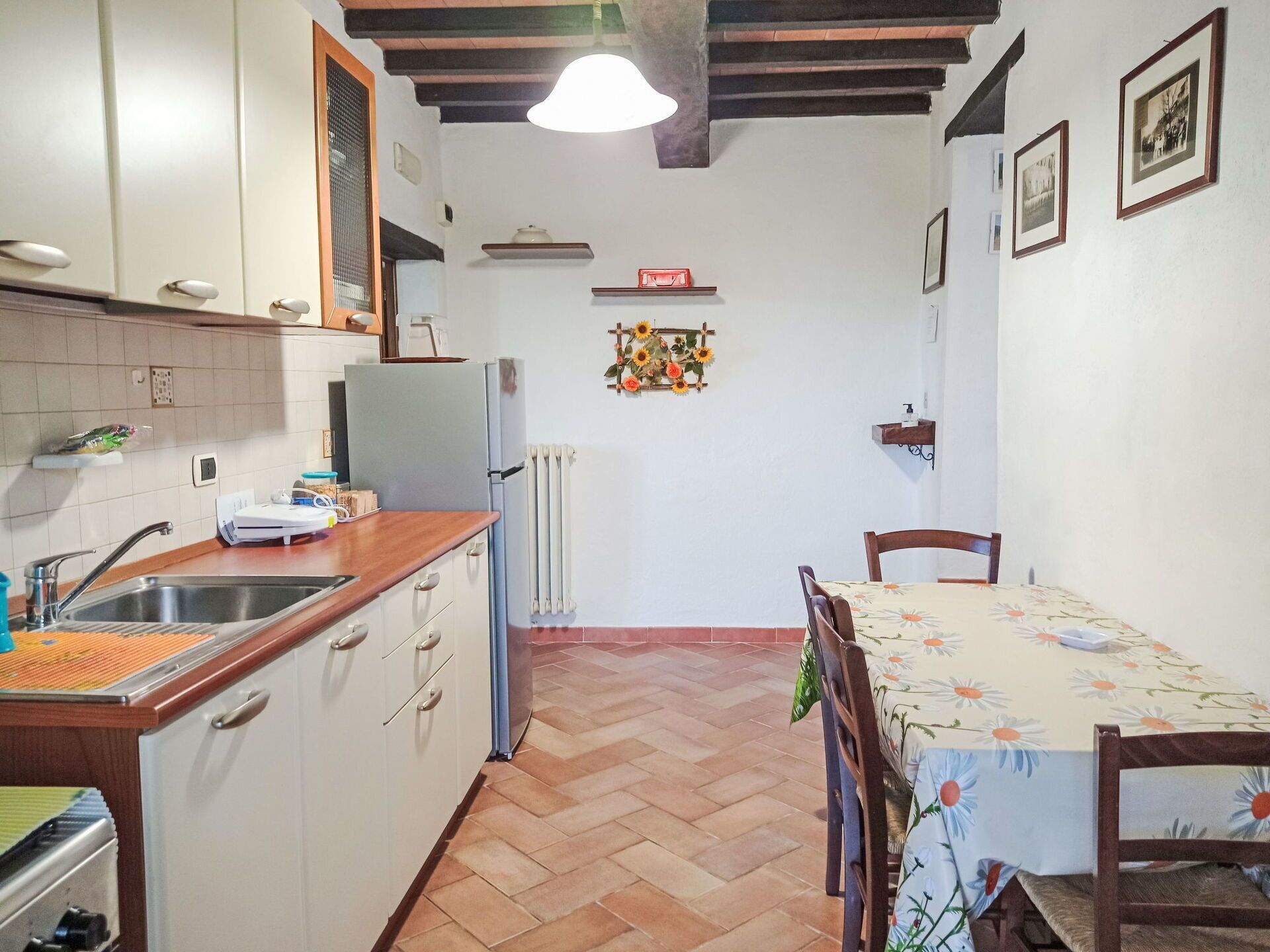 A kitchen with a sink, stove, and refrigerator. There is a dining table with chairs and a flower vase on the wall.