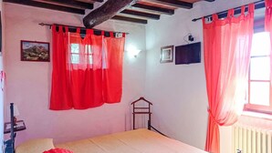 A bedroom with a bed, red curtains, a wooden ceiling, a radiator, and a small wooden shelf. - Stunning private villa for 8 people with WIFI, private pool, patio and pets allowed (Cortona)