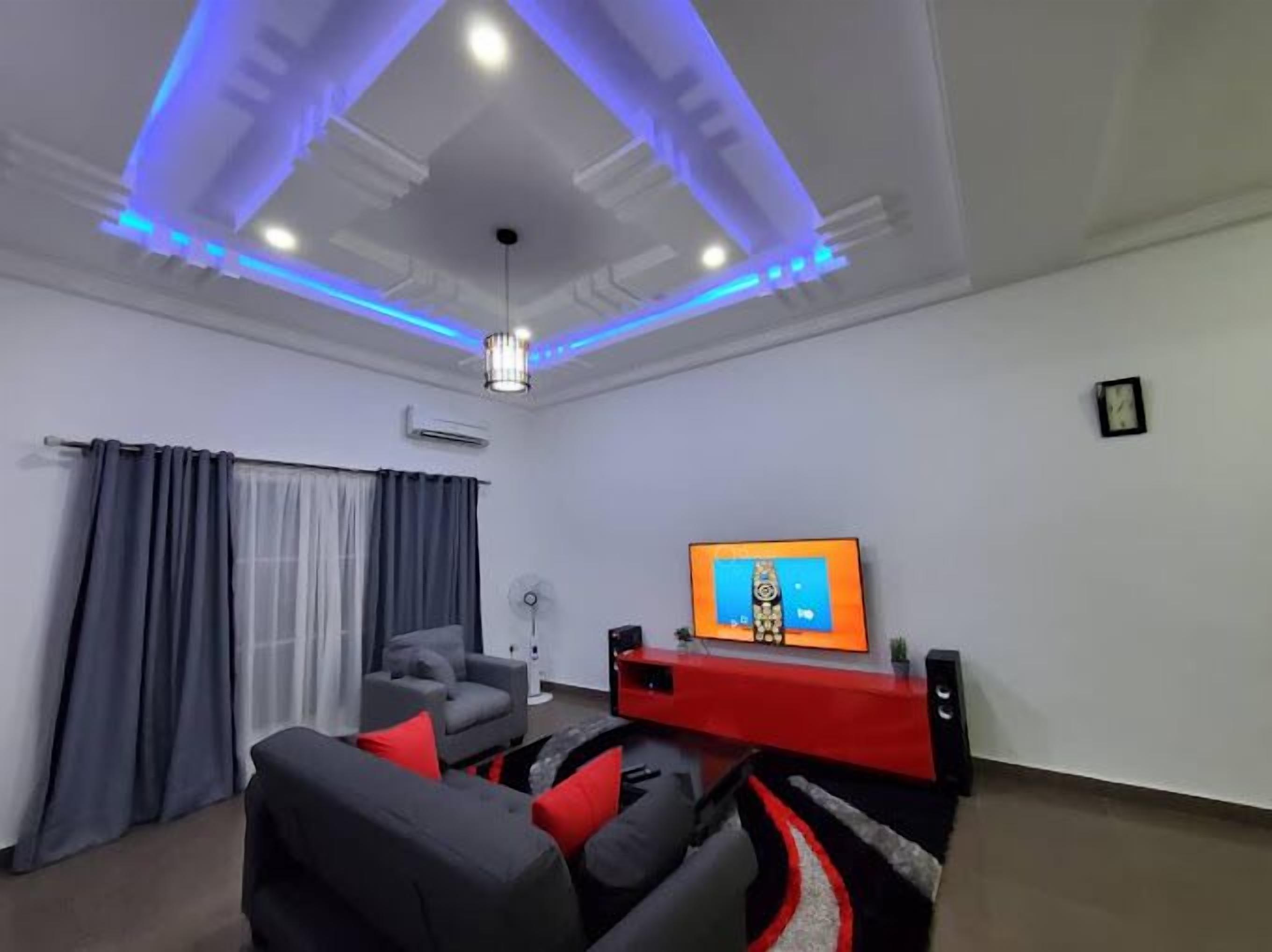 A modern living room with a flat-screen TV, a red entertainment unit, and a grey sofa with red cushions.