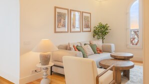 A modern living room with a sofa, a side table, a lamp, and a small wooden table. There are three framed pictures on the wall and a plant on the floor.