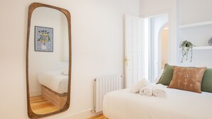 A bedroom with a large mirror, a bed with white bedding, a radiator, and a door leading to another room.