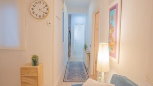 A hallway with a clock, a small cabinet with drawers, a blue rug, and a couch with a cushion. - A cozy space in Chamberí (Madrid)
