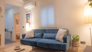 A modern living room with a blue sofa, a wooden coffee table, and a small side table with a plant. - A cozy space in Chamberí (Madrid)