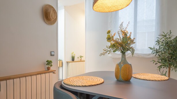 A dining area with a round table, two woven placemats, a vase with flowers, and a hat on the wall. - A cozy space in Chamberí (Madrid)
