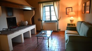 Una sala de estar acogedora con una mesa de centro de vidrio, un sofá verde, una ventana con cortinas y una lámpara sobre una mesita auxiliar.