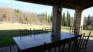 Un espacio de comedor al aire libre con una mesa y sillas de piedra, un farol y vistas a un campo de césped y árboles.