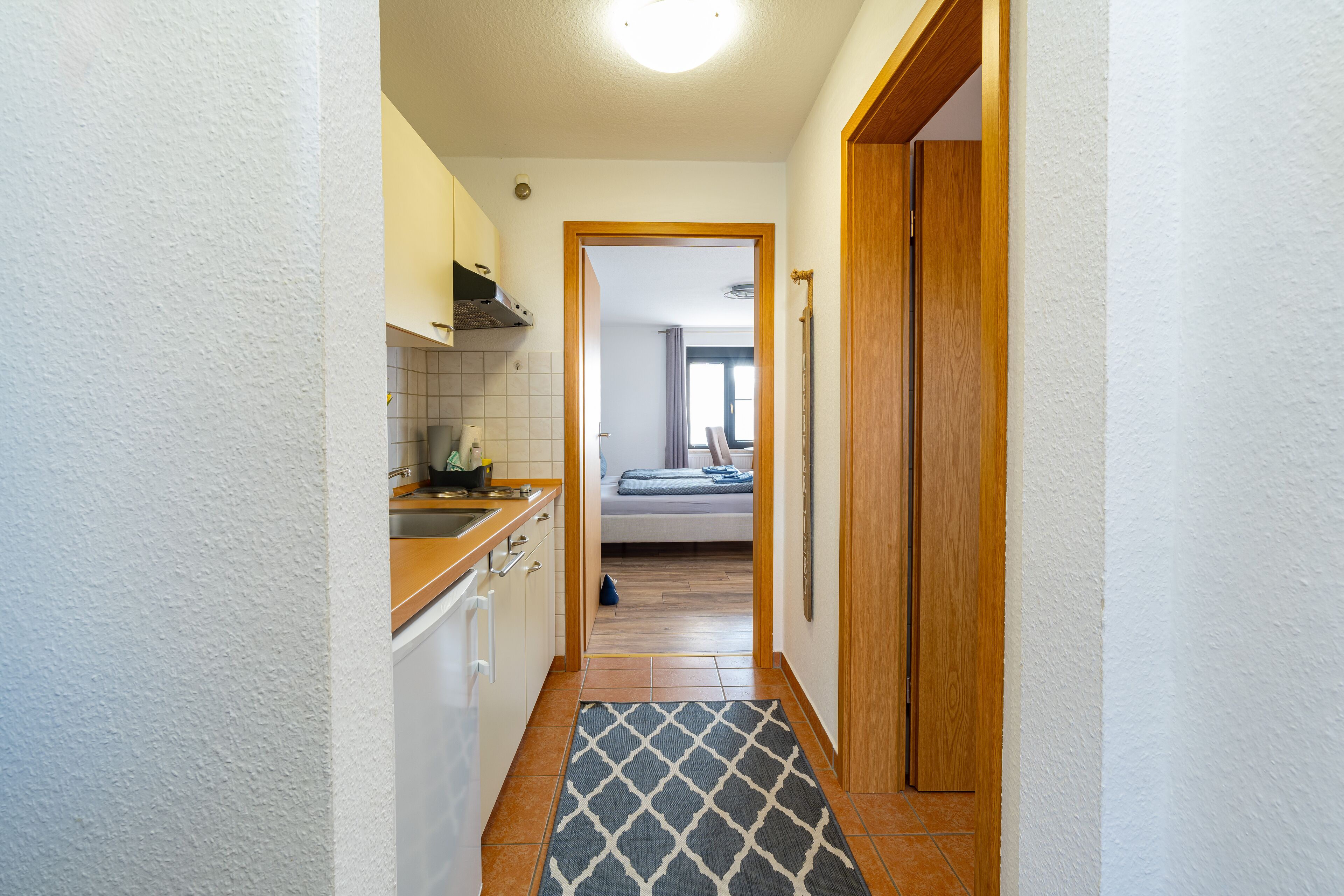 A narrow hallway with a kitchen on one side and a bedroom on the other.