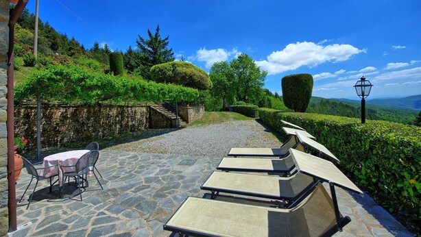 Un espace patio doté d’un sol en pierre, de sièges d’extérieur et offrant une vue sur un jardin luxuriant et des collines lointaines.