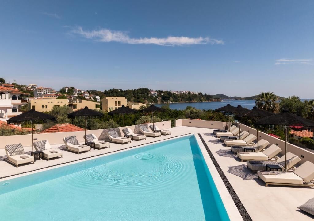 Une piscine entourée de bâtiments, dotée de chaises longues et de parasols, et offrant une vue sur la mer.