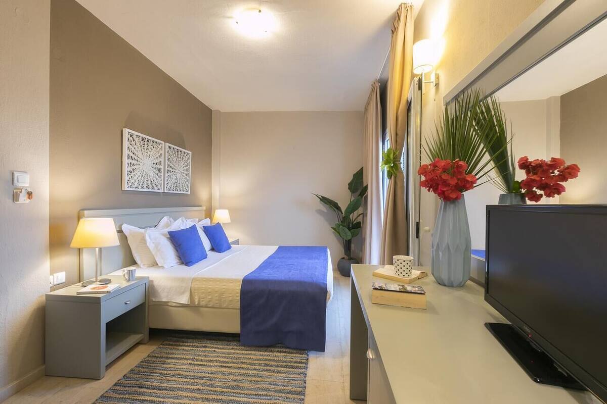A hotel room with a bed, bedside tables, a flat-screen TV, a desk, and a mirror.