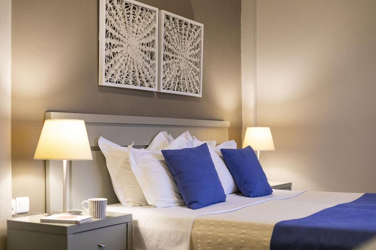 A neatly made bed with white and blue pillows, two bedside lamps, and a decorative wall piece above.