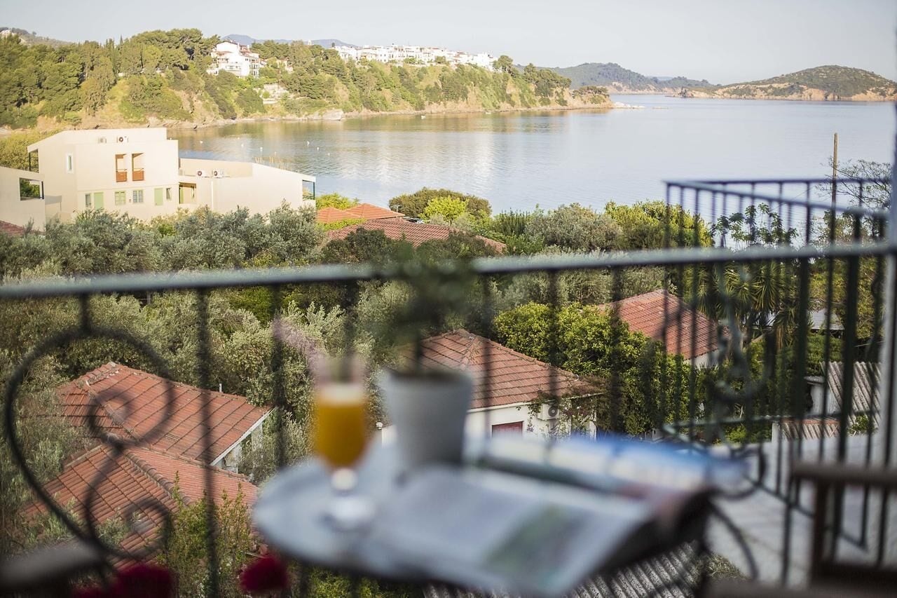 A balcony with a view of a lake, a glass of orange juice, and a newspaper.