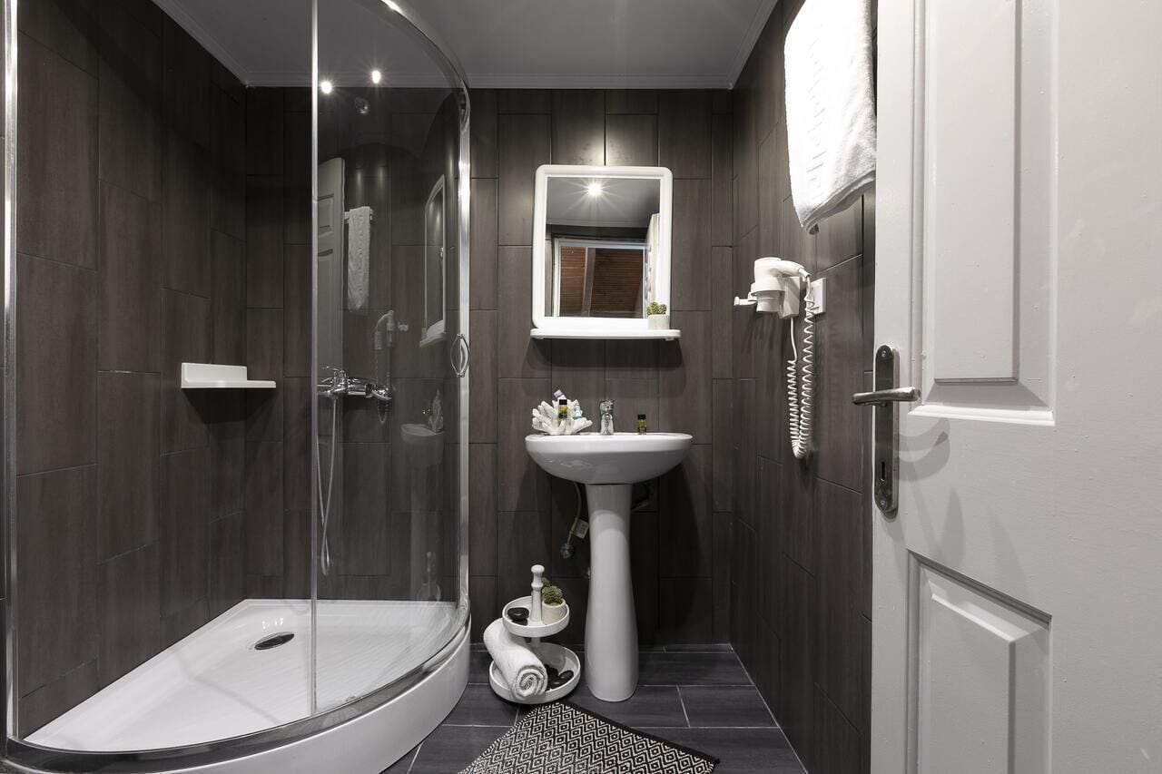 A modern bathroom with a glass-enclosed shower, a pedestal sink, and a mirror with a built-in light.