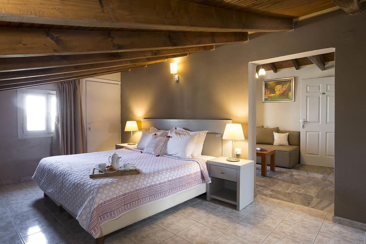 A bedroom with a bed, bedside tables, a nightstand, a window with curtains, a painting on the wall, and a door.