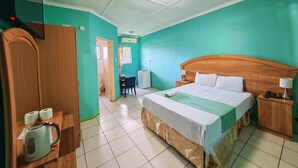 Ein Hotelzimmer mit einem Bett, einem Holzschrank, einem Schreibtisch mit Stuhl, einem kleinen Tisch mit Wasserkocher und einem durch eine offene Tür einsehbaren Badezimmer.