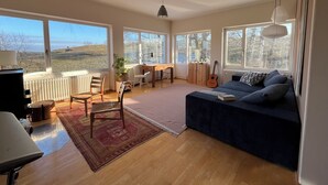 A spacious living room with large windows, a wooden floor, a blue sofa, a desk, and a guitar. - Old drawing studio in the countryside (Murnau am Staffelsee)