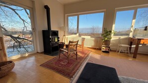 A spacious living room with a fireplace, large windows, and a view of the outdoors. - Old drawing studio in the countryside (Murnau am Staffelsee)