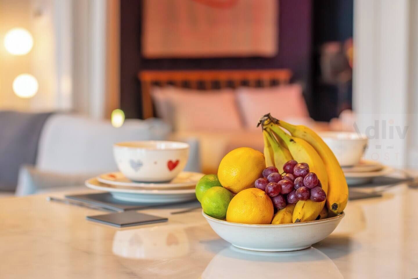 A dining table with a bowl of fruit, a cup, and a smartphone.