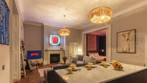 A modern living room with a fireplace, a TV displaying 'NETFLIX', and a dining area with fruit and drinks. - Historic Seaview Gem in Ramsgate by Adliv (RAMSGATE)