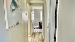 Un corridoio con pavimento in legno, pareti bianche e una porta che dà su una stanza.