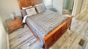 Una camera da letto con un letto di legno, un comodino, una finestra e una porta che dà su un bagno.