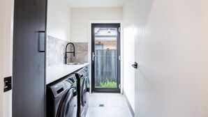 A narrow hallway with a washing machine and a sink on one side, leading to a door with a view of a garden. - Modern 3B house, pet friendly close nature reserve (Throsby)
