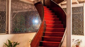 A spiral staircase with red steps leading to a landing, flanked by potted plants and decorative metal grilles. - amã Stays & Trails Hathikuli, Assam (Bokakhat)