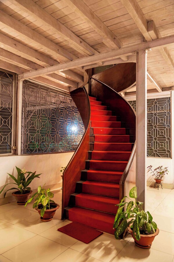 A spiral staircase with red steps leading to a landing, flanked by potted plants and decorative metal grilles. - amã Stays & Trails Hathikuli, Assam (Bokakhat)