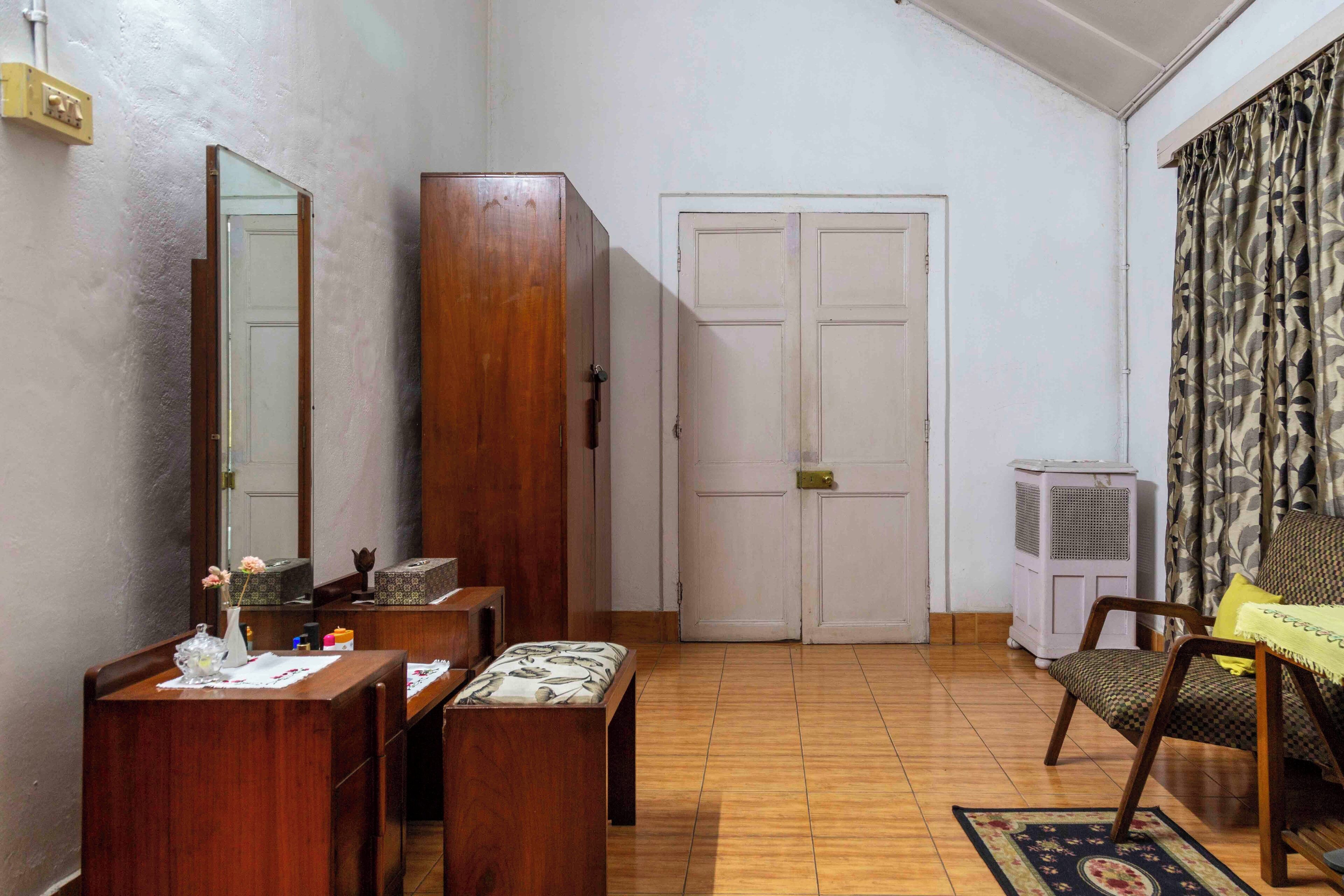 A room with a wooden desk, a mirror, a wardrobe, a door, and a chair with a cushion.
