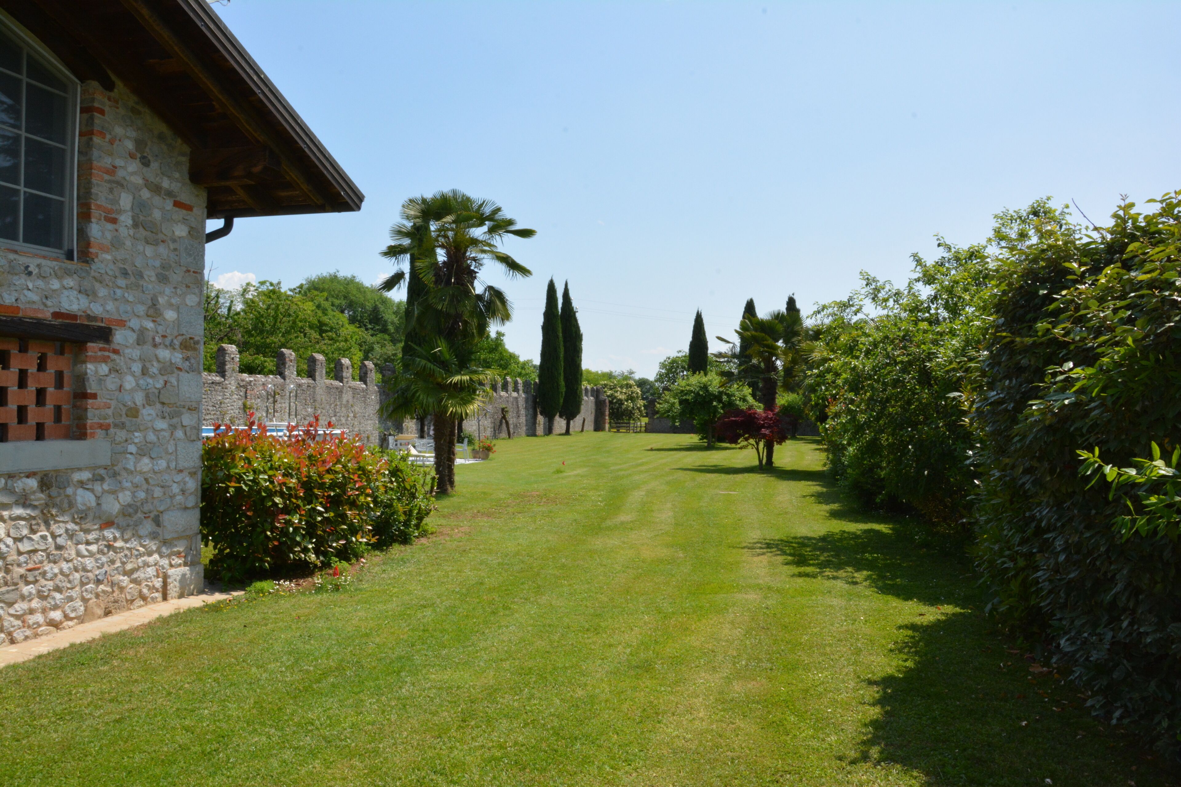 A stone building with a brick section, a well-maintained lawn, and a stone wall with a gate.