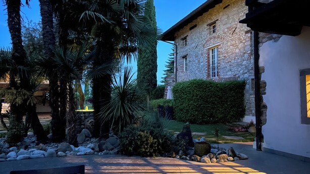 A courtyard with a stone building, palm trees, and a bench. - Residence San Bernardo - Ap. "San Bernardo" - 6 km from the center of Udine (Udine)