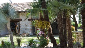 A stone building with a tiled roof, surrounded by a garden with palm trees and flowering plants. - Residence San Bernardo - Ap. "San Bernardo" - 6 km from the center of Udine (Udine)