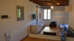 A modern hotel room with a wooden ceiling, a dining area with a table and chairs, a built-in TV, a radiator, and a window with blinds. - Residence San Bernardo - Ap. "San Bernardo" - 6 km from the center of Udine (Udine)