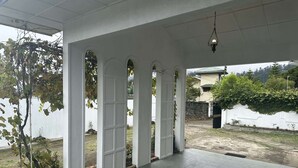A covered outdoor area with white columns and a tiled floor. - Cottage 88 (Nuwara Eliya)