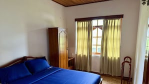 A bedroom with a wooden bed, a wardrobe, a window with curtains, and a wooden chair. - Cottage 88 (Nuwara Eliya)