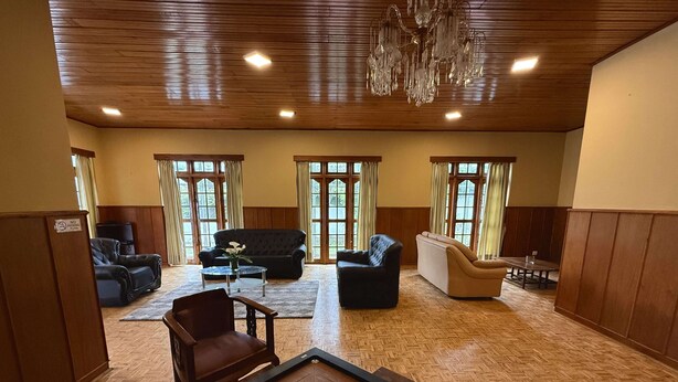 A spacious living area with a wooden floor, multiple seating options including sofas and chairs, a coffee table, and a chandelier. - Cottage 88 (Nuwara Eliya)