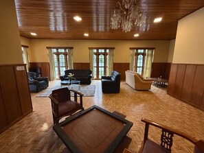 A spacious living area with a wooden floor, multiple seating options including sofas and chairs, a coffee table, and a chandelier. - Cottage 88 (Nuwara Eliya)