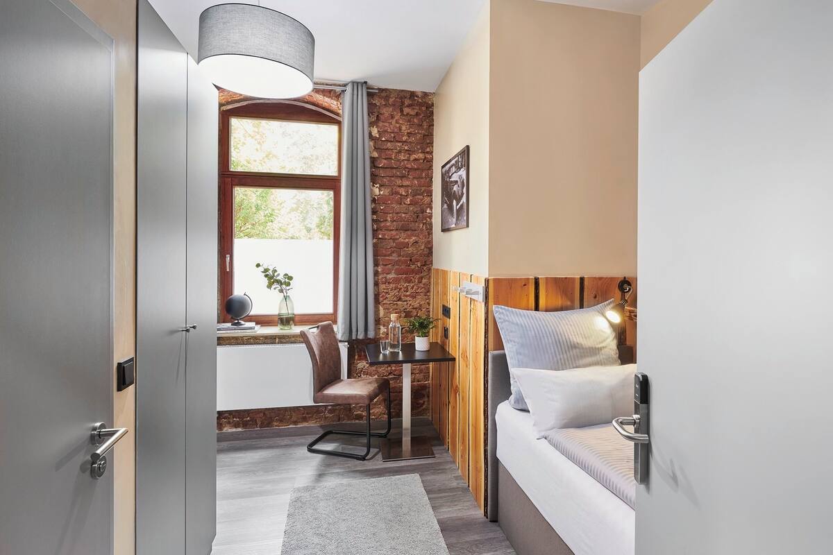 A modern room with a brick wall, a wooden headboard, a desk with a chair, and a bed with a headboard.