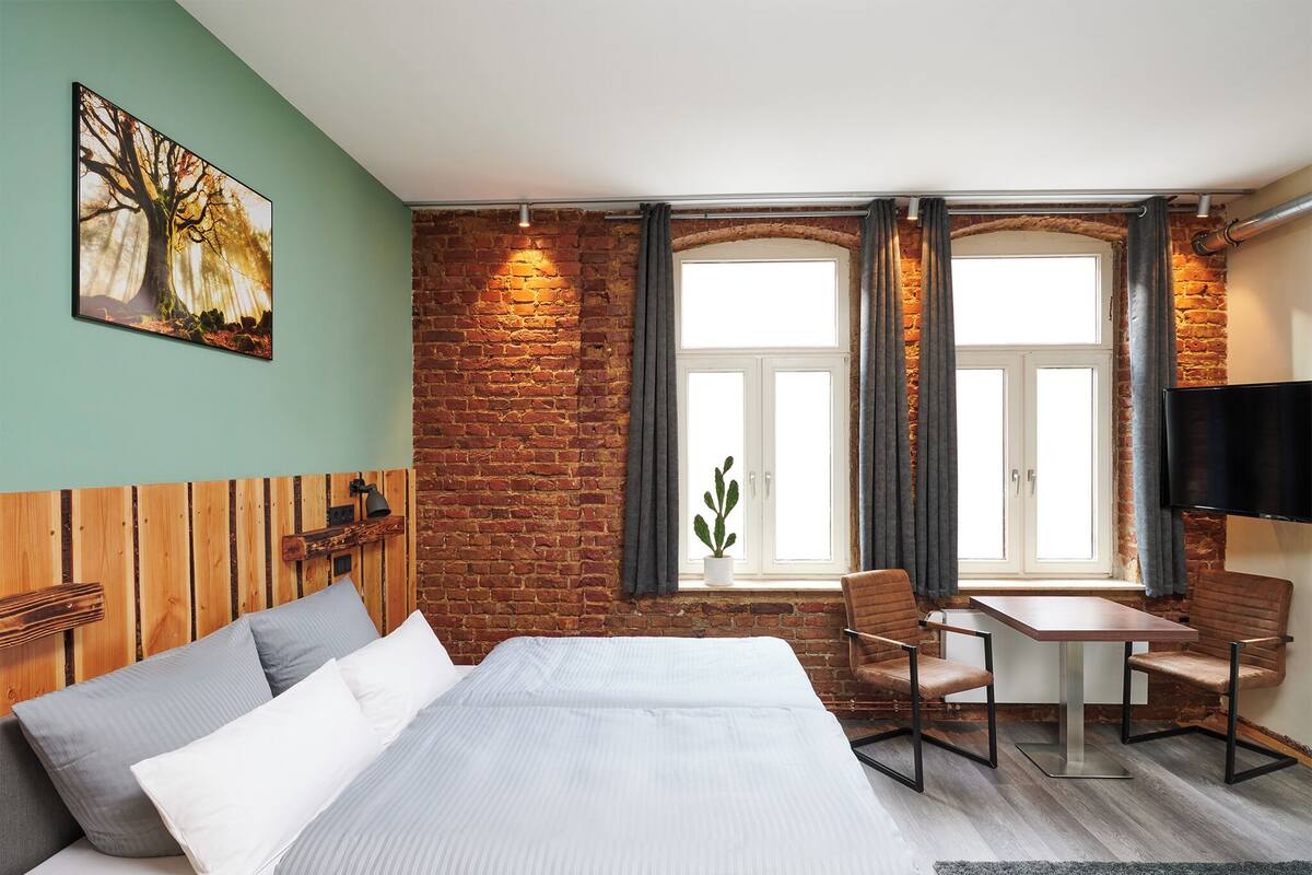 A hotel room with a bed, a desk, a chair, a TV, and a window with curtains.