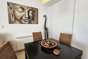 Un comedor con una mesa negra, sillas de mimbre, un cuenco de nueces y una corbata con estampado de jirafa colgada en la pared.