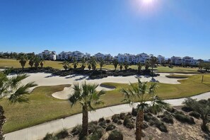 Campo de golf con búnkeres de arena, palmeras y una hilera de edificios blancos al fondo.